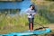 Active woman inflates SUP board with manual pump, beautiful lake and nature on background, stand up paddling water adventure