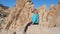 Active Woman Sits High On The Edge Of The Rock, Rejoicing The View And Smiling