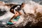 Active woman stands with bent knees on surf style wakeboard and ride on wave