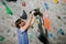 Active young bearded man in glasses building climbing wall with color holds indoors using drill tool