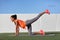 Active young fit woman doing bodyweight glute leg exercise on outdoor grass. Fitness girl exercising donkey kick strength training