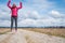 Active young woman jumping high on dirt road surrounded with fields.