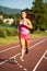 Active young woman runs on atheltic track on summer afternoon