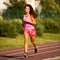 Active young woman runs on atheltic track on summer afternoon