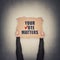 Activist hands holding up a cardboard banner with text message your vote matters, isolated on gray wall background. People legal