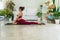 Activity women sitting on mat in front of white sofa while doing position yoga Anjaneyasana in living room. Relaxation girl