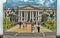 Administrative building with stucco on the facade against the background of walking people on the alley with benches and