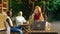 An admirable woman with long ginger hair is at a table near a cafe in the park, she is in deep conversation on her phone