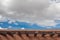 Adobe roofline with exposed vigas and open latillas, blue sky with clouds