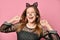 Adolescent in black dress, headband like cat ears, face painting. She posing on pink background. Close up