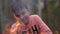 Adolescent boy looking with antipathy through line of fire flame in forest.