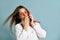 Adolescent in orange sunglasses, watch, bracelet and sweater. She talking by phone, surprised, posing on blue background. Close up