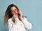 Adolescent in orange sunglasses, watch, bracelet and sweater. She talking by phone, surprised, posing on blue background. Close up