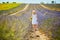 Adorable 4 year old girl in white dress and straw hat walking through rows of lavender near Valensole, France