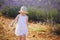 Adorable 4 year old girl in white dress and straw hat walking through rows of lavender near Valensole, France