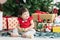 Adorable 8 months Asian baby girl smiling and having fun playing toy, sitting in front of a Christmas tree on floor
