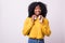 Adorable african woman in yellow sweater singing and having fun while listening to music using wireless earphones  over