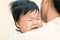 Adorable asian baby sick and crying on mom shoulder.