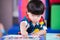 Adorable Asian boy reached for pick up chalk paint, baby made art on the paper placed on the table. Child learn crafts at home.
