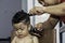 Adorable baby boy having a haircut by his father at his home