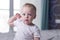 Adorable baby boy scratching behind the ear and looking at camera. Blue-eyed calm infant kid. Close-up portrait