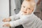 Adorable baby with calm face expression that leans on windowsill