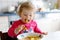 Adorable baby girl eating from fork vegetables and pasta. food, child, feeding and development concept