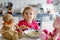 Adorable baby girl eating from fork vegetables and pasta. Little child feeding and playing with toy doll