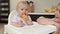Adorable baby girl eating orange. Little daughter sitting in feeding chair and eating slice of orange at kitchen and