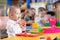 Adorable baby playing with educational toys with group of nursery kids under teacher supervision