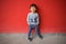 Adorable baby in stylish clothes posing in front of red wall