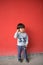 Adorable baby in stylish clothes posing in front of red wall
