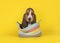 Adorable basset hound puppy dog sitting in a multi colored basket on an yellow background