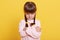 Adorable beautiful little offended girl isolated over yellow background, dresses casually, looks from under forehead with angry