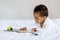 Adorable Black Baby Boy Or Girl Reading Book While Lying On Bed