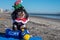 An adorable black and white Havanese puppy posing in Christmas outfit and hannukkah toys on a blue towel on the beach at the edge