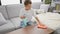 Adorable blond boy comfortably sitting on sofa, concentrating on cleaning table in the cozy living room at home