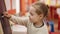 Adorable blonde girl preschool student writing on blackboard at kindergarten