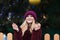 Adorable blonde woman dressed in knitted hat and warm coat holding glowing sparklers at the Christmas tree