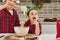 Adorable boy kneads dough with a wooden spoon when his cute younger sister climbs her hands into the dough and tastes it. Charming