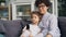 Adorable boy and mother young woman watching TV and talking at home on sofa