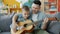 Adorable boy playing the guitar under guidance of caring father learning at home