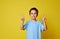 Adorable boy posing into the camera over yellow background with copy space. Child gesturing victory with fingers