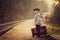 Adorable boy on a railway station, waiting for the train with suitcase and teddy bear