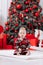 Adorable caucasian baby boy is sitting and holding gift toy Santa Claus near a Christmas tree, many festive gift boxed