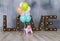 Adorable caucasian baby girl with colorfull balloons creeps on wooden floor at studio