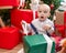 Adorable caucasian baby unpacking gift sitting on floor by christmas tree at home