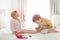 Adorable Caucasian boy and girl siblings playing together painting nails pedicure sitting on bed at home.