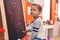 Adorable caucasian boy preschool student sitting on chair drawing on blackboard at kindergarten