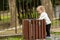 Adorable caucasian child looking into a trashcan with curiosity on a spring day. Cute blonde kid exploring the world around him in